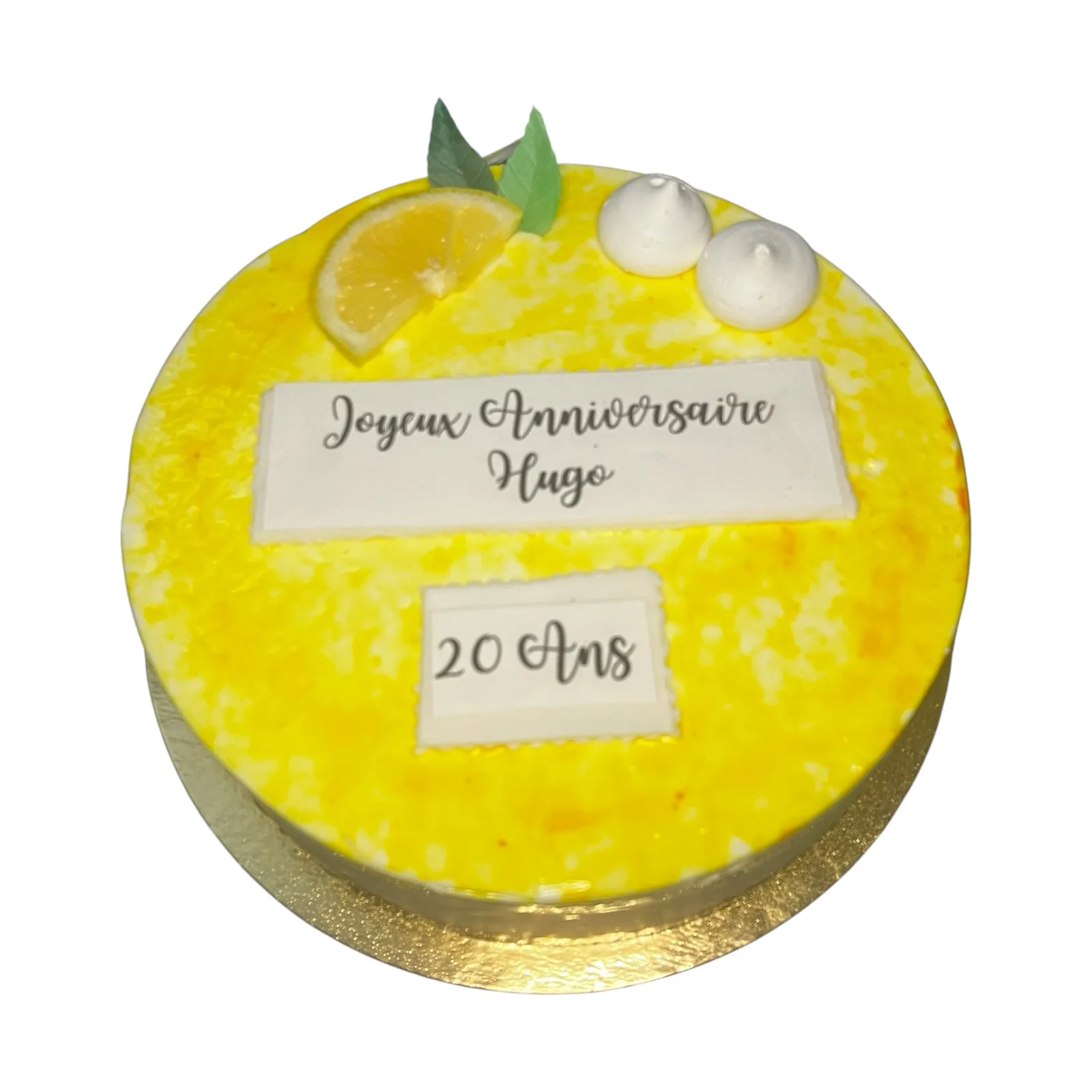 Entremets rond au glaçage citron, décoré d'un quartier de citron frais et de meringues, message « Joyeux Anniversaire Hugo, 20 Ans »