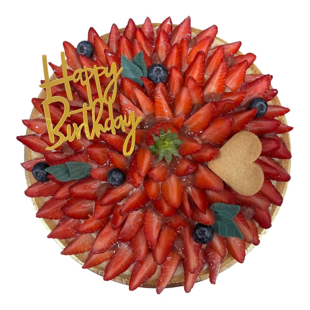 Tarte ronde recouverte de fraises et myrtilles fraîches, topper doré Happy Birthday et biscuit en forme de cœur