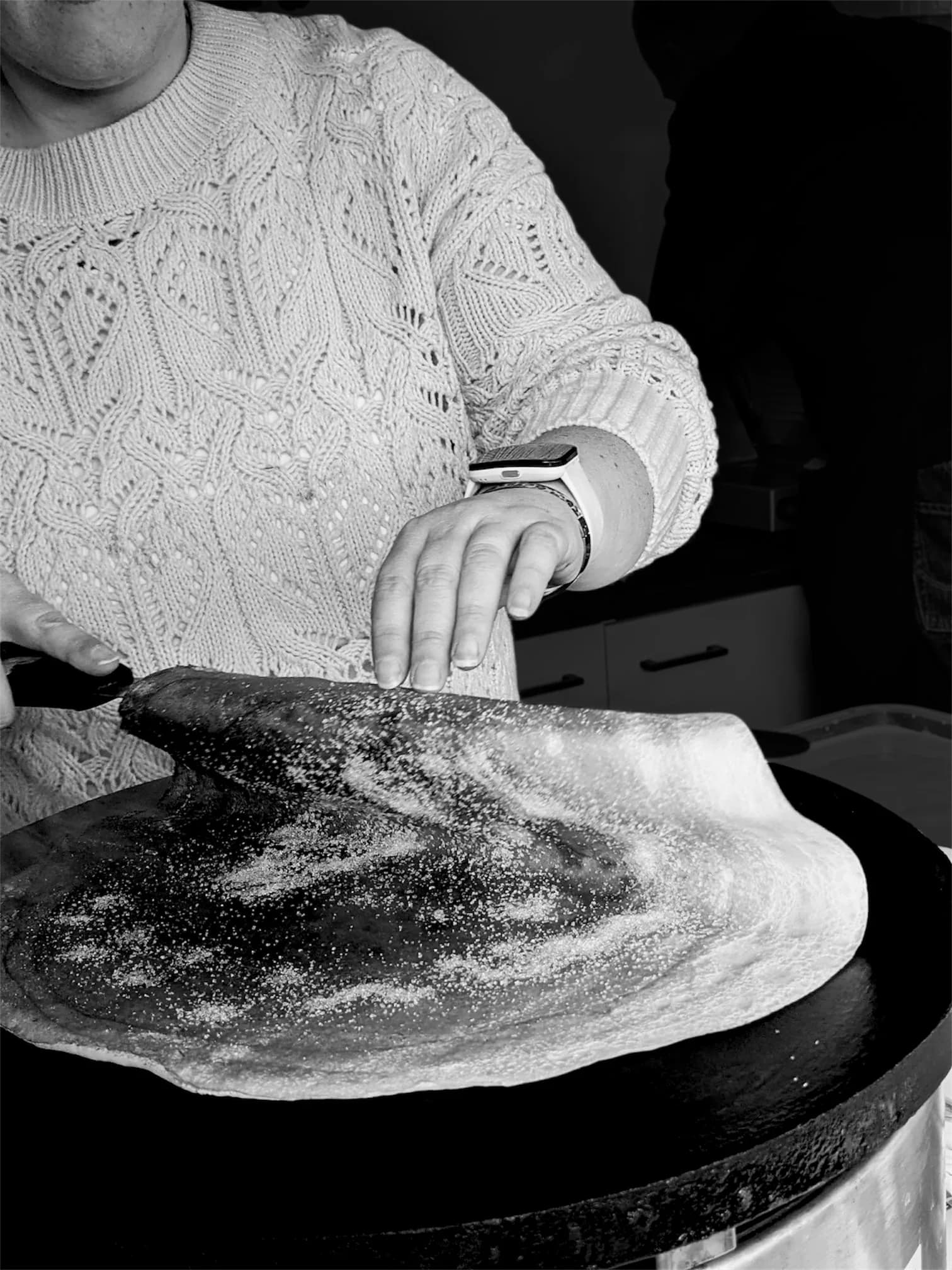 Julie étalant la pâte à crêpe au rateau sur une crêpière traditionnelle, photo en noir et blanc